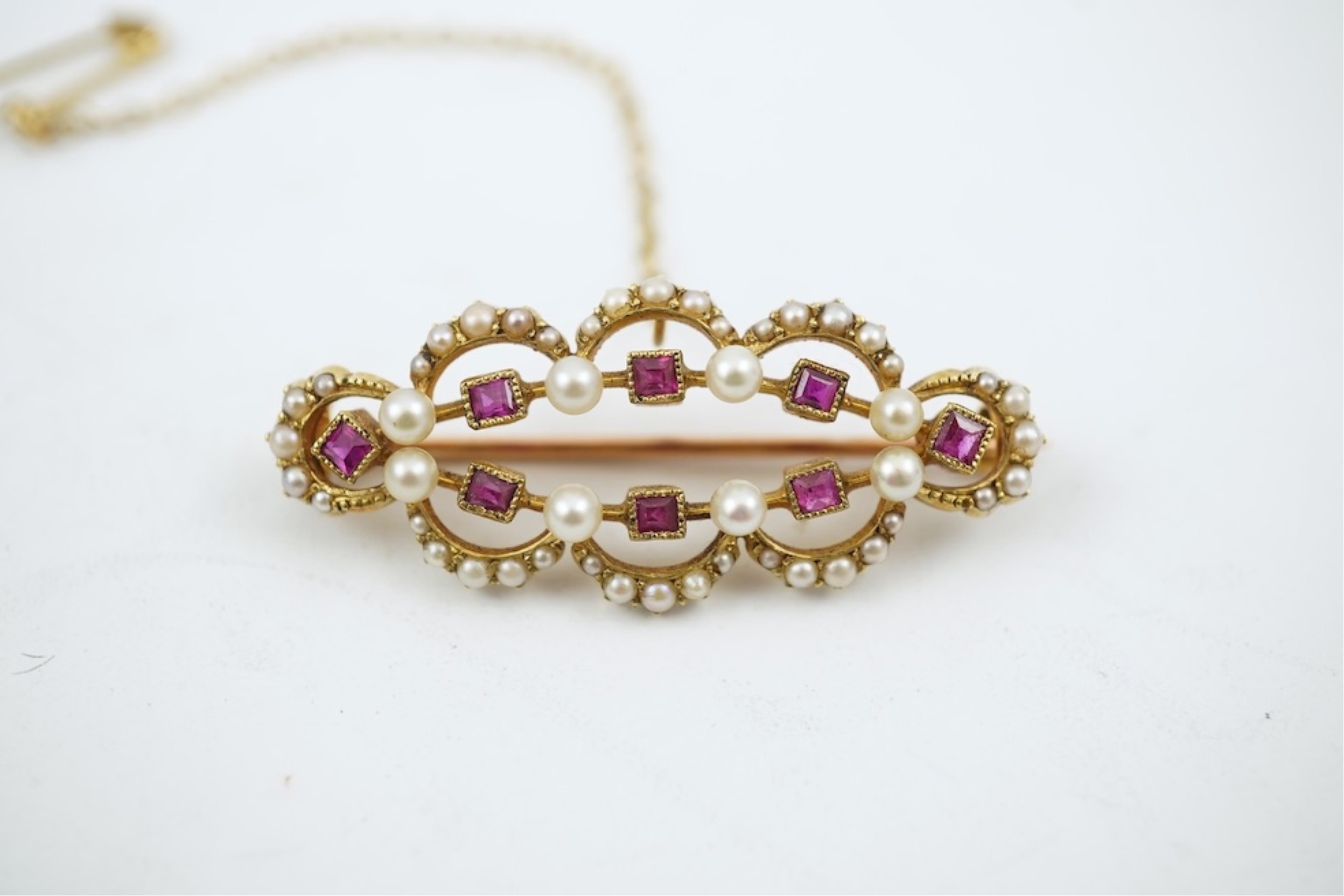 An Edwardian 15ct, ruby and seed pearl cluster set brooch, 33mm, with safety chain, gross weight 4.1 grams.
